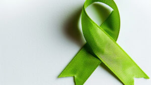 Green awareness ribbon symbolizing mental health and kidney donation on a light background